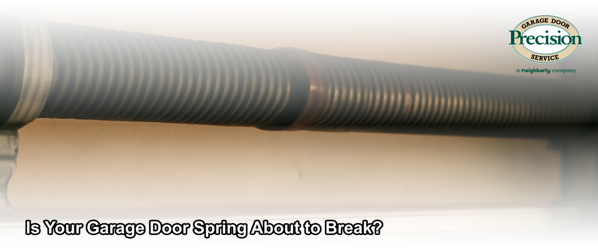 Close-up of a torsion spring above a residential garage door showing visible wear and rust, indicating it may be near failure